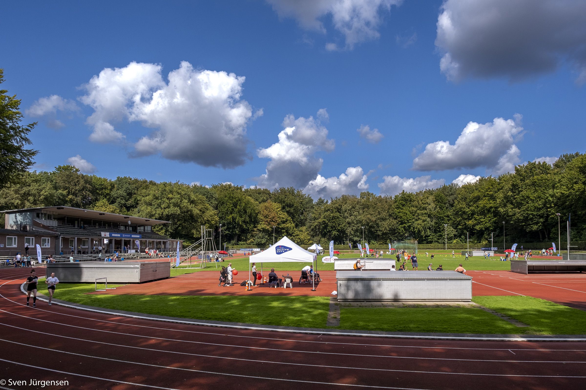 Bild eines Sportplatzes bei blauem Himmel. Auf dem Sportplatz sind verschiedene Aktivitäten aufgebaut.