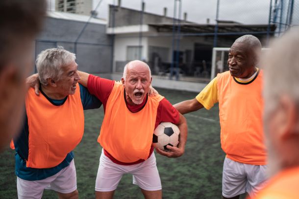 Ein älterer Mann hält eine motivierende Rede für das Senioren-Team auf dem Fußballfeld.