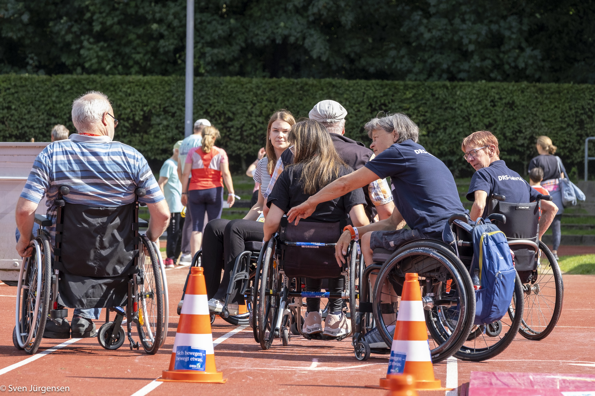 Eine Gruppe Menschen in unterschiedlichen Alter im Rollstuhl steht auf einem Sportplatz